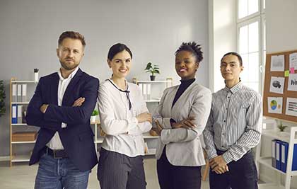 A smiling group of co-workers standing in an office with their arms crossed or hands clasped together