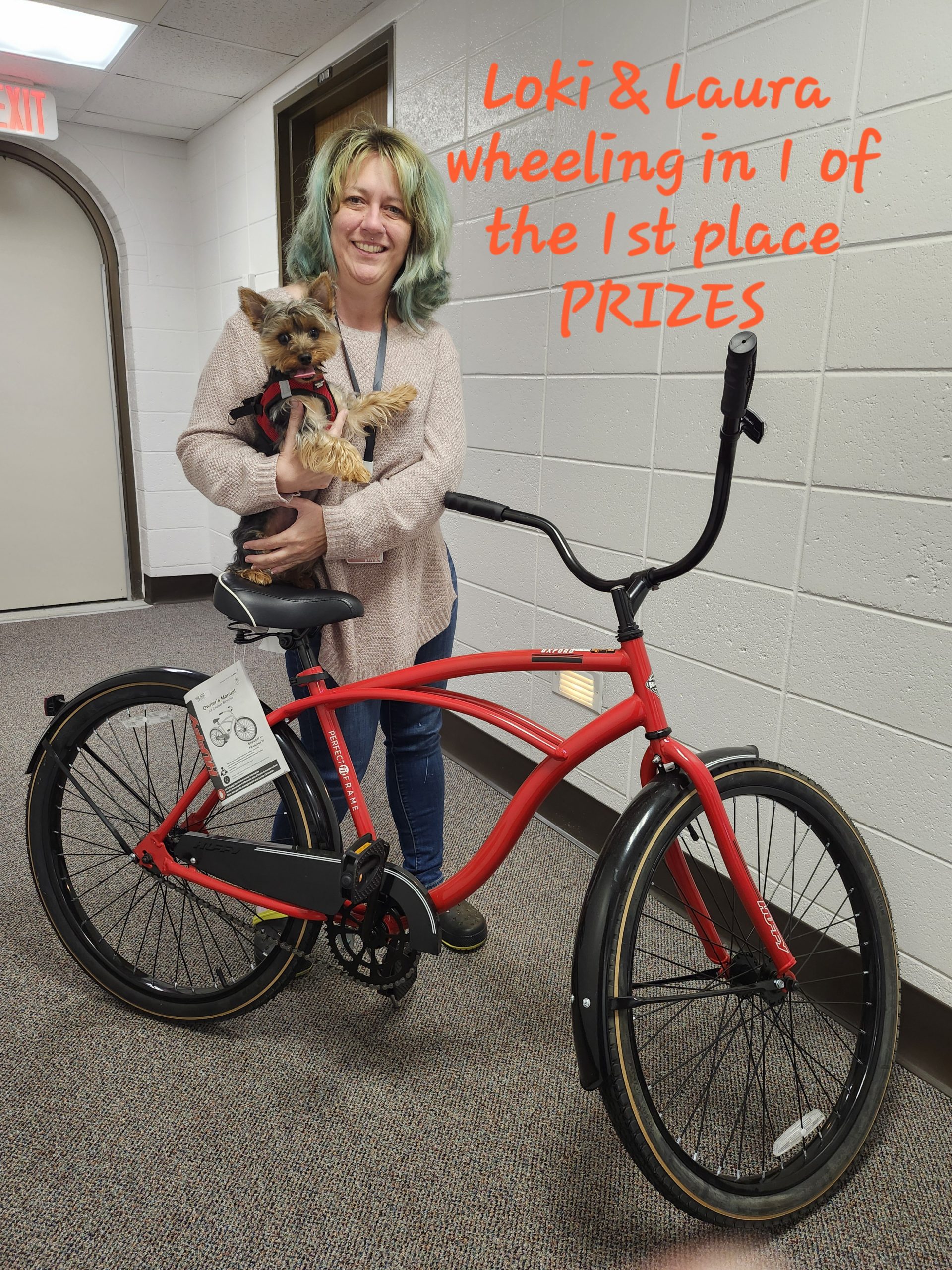 A woman smiles while holding her dog, the first-place winner of the Cutest Pet Photo Contest. Next to her is the prize, a bright red bike.