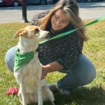 A woman leans down to pet a smiling dog wearing a green scarf during the PAWS for People De-Stress event.