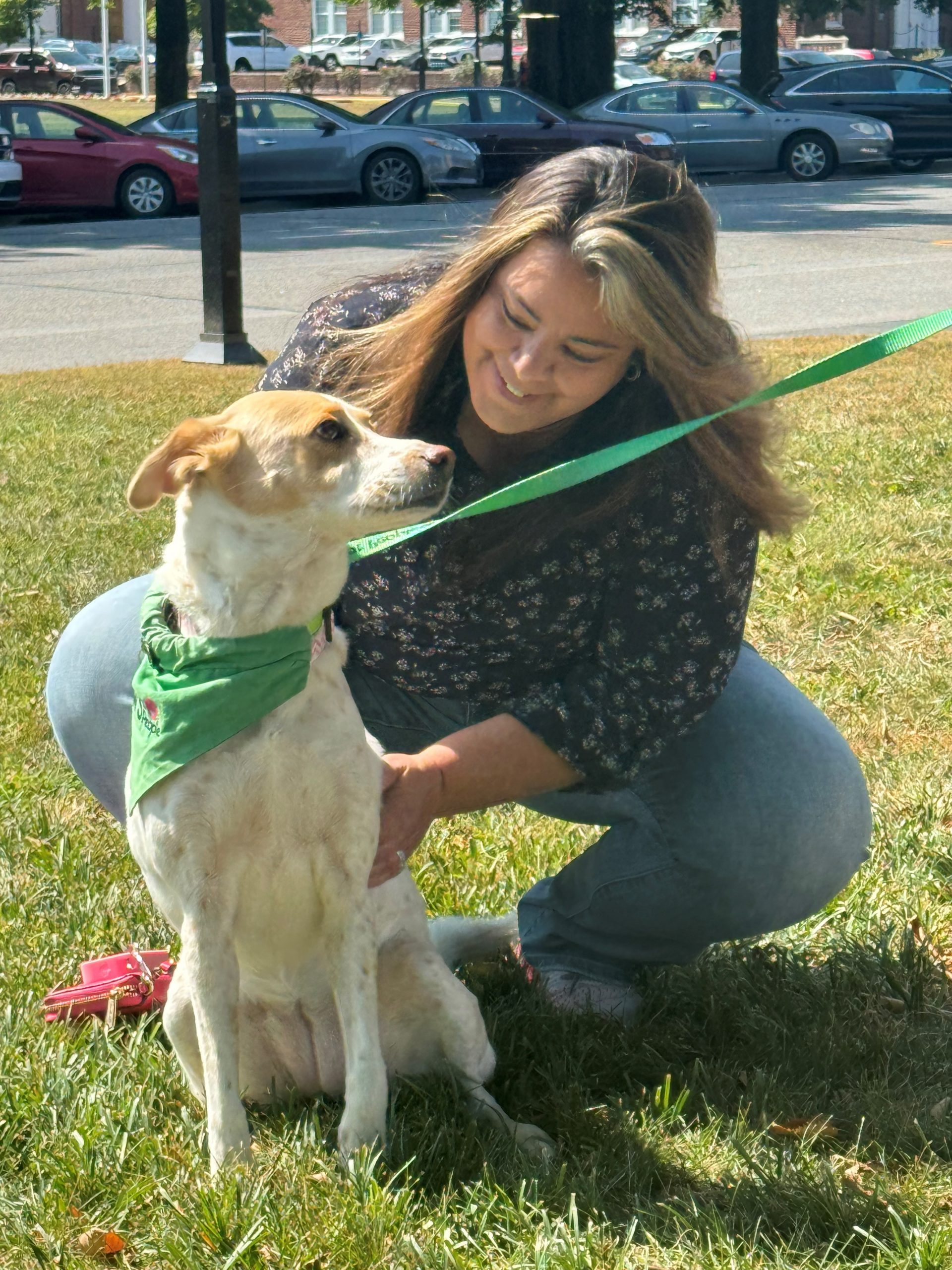 A woman leans down to pet a smiling dog wearing a green scarf during the PAWS for People De-Stress event.