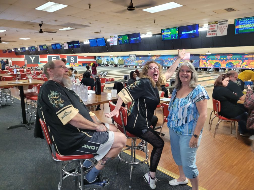 3 people enthusiastically posing for a photo in a bowling alley