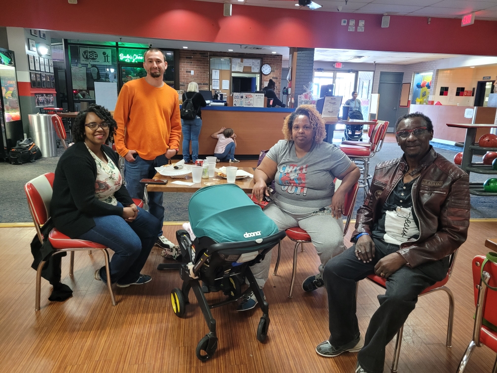 3 People Smiling at a bowling alley table 1 person standing behind them