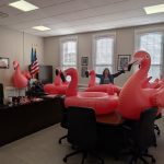 DHSS Secretary Manning holds her arms up with a smile while surrounded by six inflatable giant flamingo pool floats.