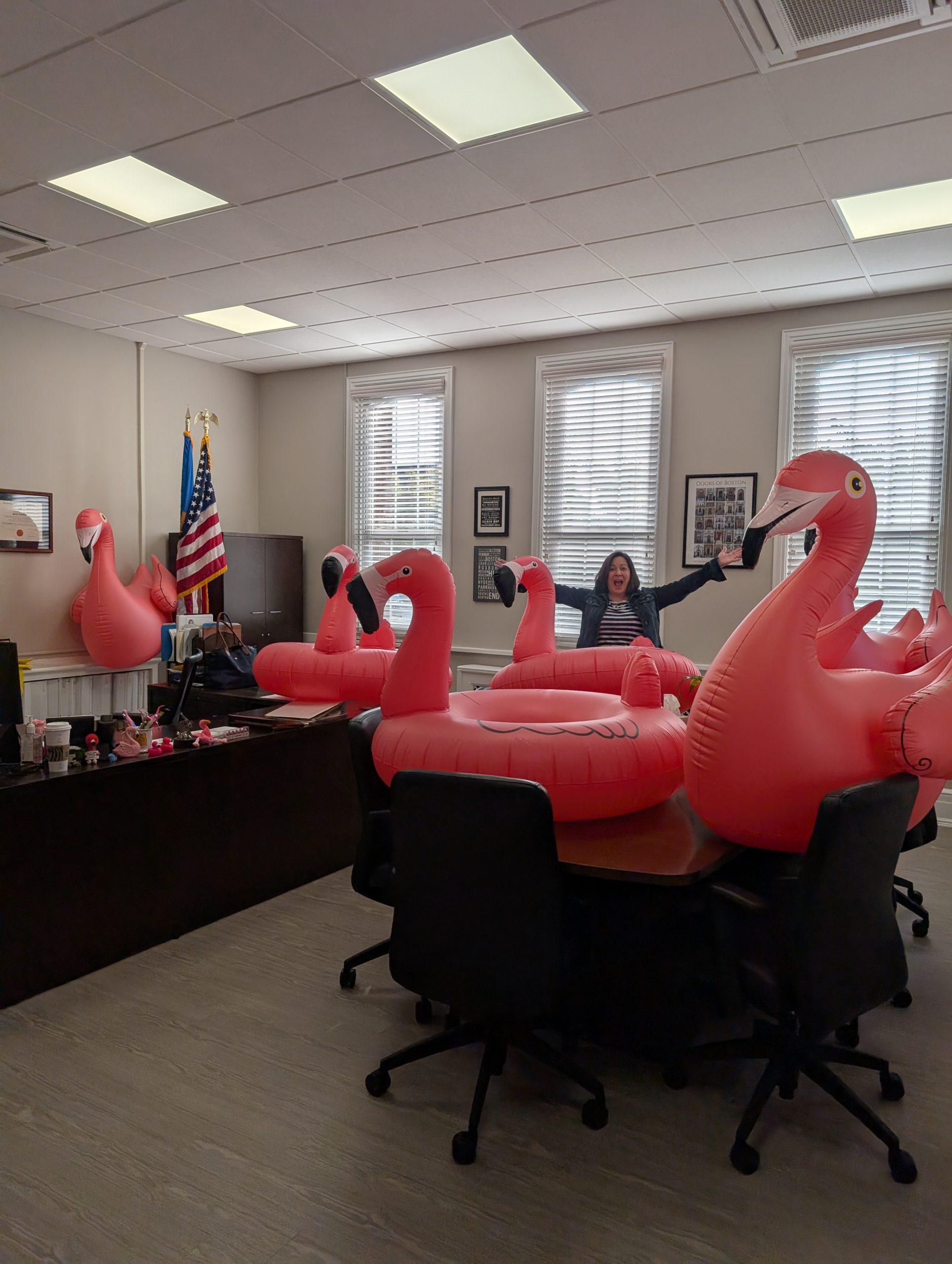 DHSS Secretary Manning holds her arms up with a smile while surrounded by six inflatable giant flamingo pool floats.